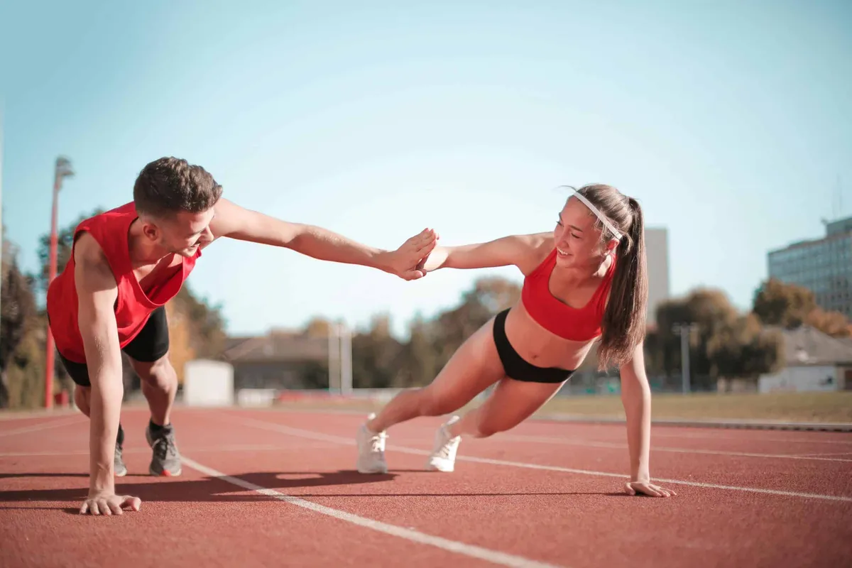 male and female athlete high fiving one another in red tops with black bottoms before their track race